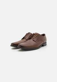Chaussures habillées en cuir brun avec un bout arrondi, un design à lacets et une texture lisse. Dotées d'une semelle en caoutchouc noir et de détails de couture minimaux.