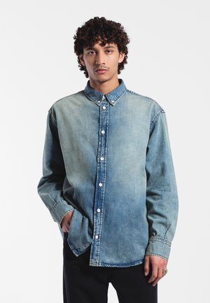 Light blue denim shirt with a button-down collar, long sleeves, and a gradual color fade, featuring large front buttons and side pockets.