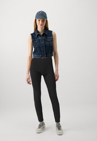 Jeans prerezani prsluk s dugmadi, crne tajice visokog struka i sive tenisice. Plava kapa i naušnice na obruče upotpunjuju izgled.