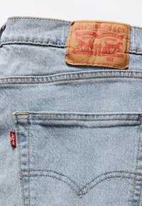 Hellblaue Jeans aus Denim zeigen ein braunes Lederetikett mit rotem Text und einer Grafik von zwei Pferden am Bund sowie ein rotes Levi's-Label an der Tasche.
