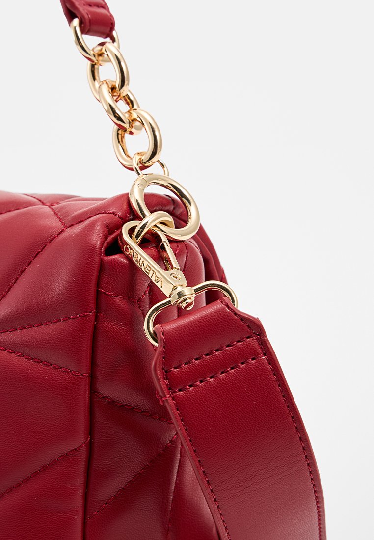 Bolso de cuero acolchado rojo con cadena dorada y herrajes. Cuenta con una correa desmontable y un intrincado bordado a lo largo de los bordes.
