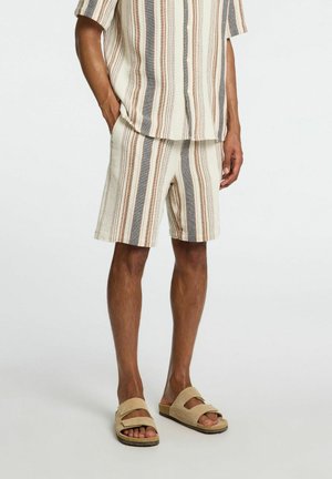 Camicia a maniche corte con bottoni e pantaloni corti in un motivo a righe di crema, marrone e grigio; abbinata a sandali beige.