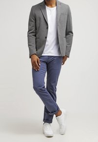 Grå kavaj med två knappar över en vit t-shirt, matchad med blå byxor och vita sneakers. Slät tyg, skräddarsydd passform och uppvikta ärmar.