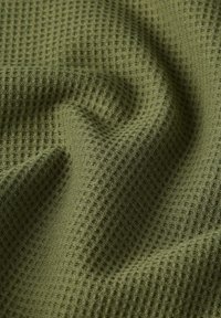 Primer plano de tela de color verde oliva con textura de gofre, con pliegues suaves y sombras que muestran su textura y caída.