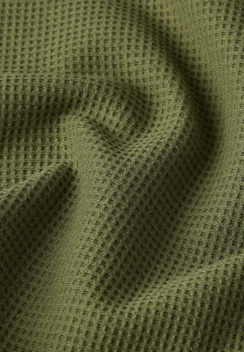 Primer plano de tela de color verde oliva con textura de gofre, con pliegues suaves y sombras que muestran su textura y caída.