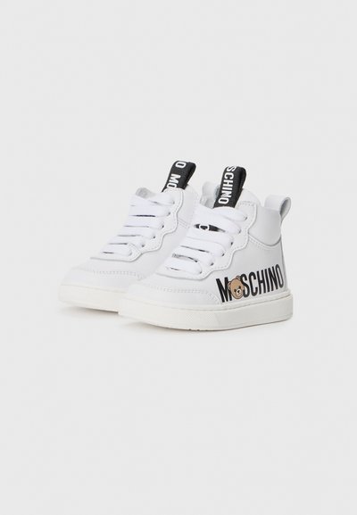 Witte hoge sneakers van glad leer met zwarte branding, vetersluiting en een cartoonbeeraccent aan de zijkant.