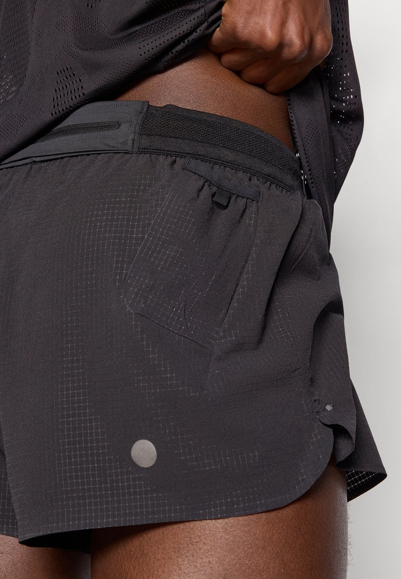 Shorts de sport noirs avec une taille ajustée, motif texturé et détail de poche latérale. Équipés de matériel réfléchissant sur le bord inférieur.