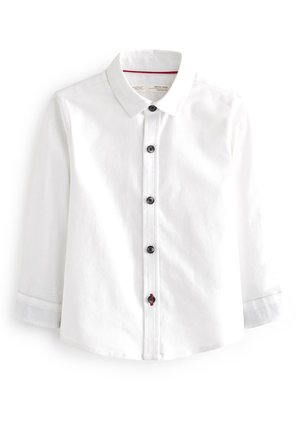 Chemise blanche à manches longues avec boutons noirs, un col et un détail de couture rouge sur le bouton du bas.