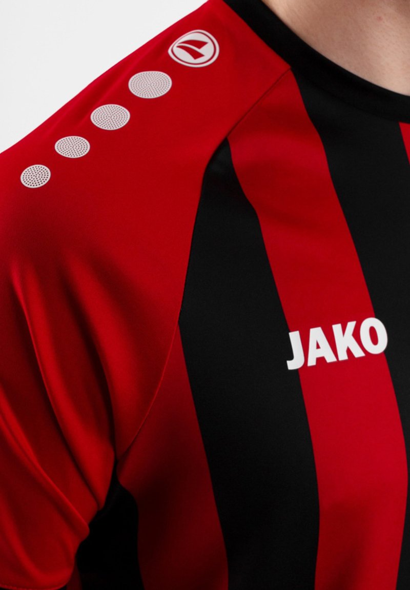 Maglia sportiva a righe rossa e nera con una texture liscia; presenta il marchio bianco "JAKO" e accenti circolari sulla spalla.