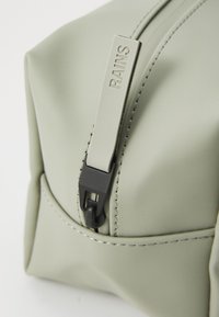 Light green waterproof pouch with a smooth texture, featuring a black zipper pull with the word "RAINS" embossed. Seam detailing visible.