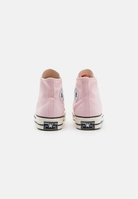 Rosa kanvas høye sneakers har en sirkulær logo-patch, svart og hvit stripete gummisåle, og et teksturert stoffoverdel.