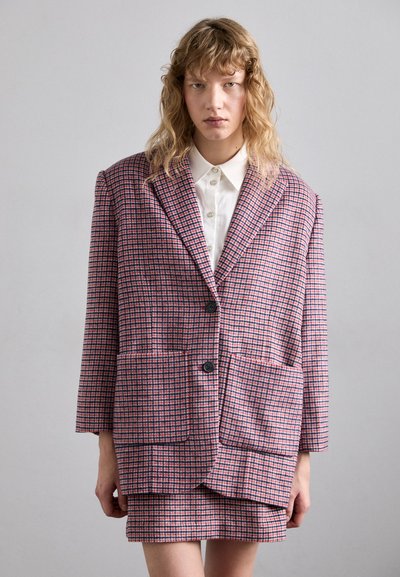 Blazer de cuadros de gran tamaño en rosa y azul marino, con grandes bolsillos frontales, un cierre de un solo botón y una tela texturada. Estilizado con una camisa blanca.