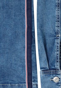 Gros plan sur un tissu denim bleu avec des détails de bordure rouge, blanche et bleue et un bouton métallique sur un poignet de manche.