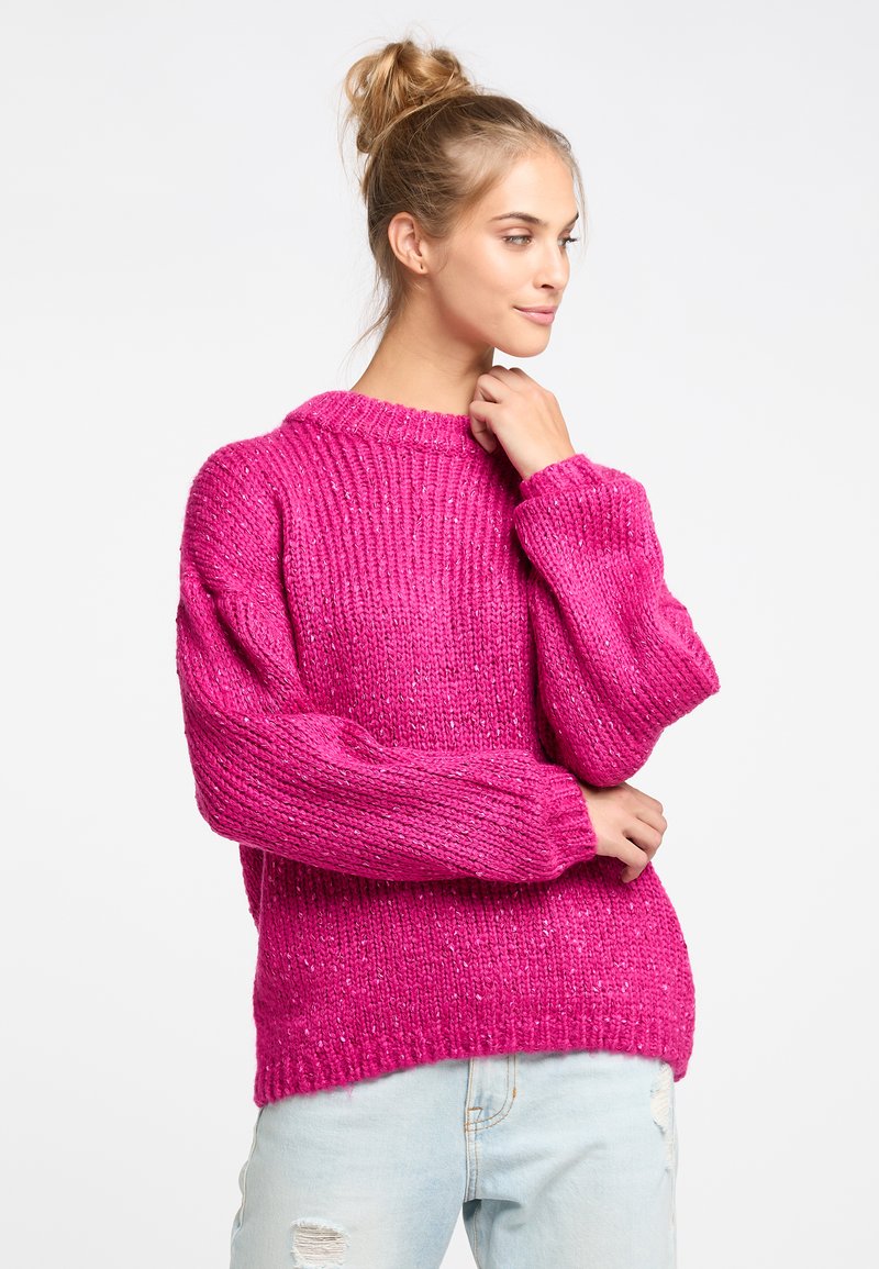 Maglione a maglia rosa con un motivo testurizzato, vestibilità rilassata e maniche larghe. Abbinato a jeans chiari strappati.