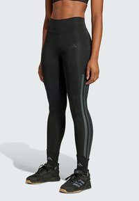 Leggings neri a vita alta con una texture liscia, caratterizzati da tre strisce verticali scure sui lati e cuciture piatte per un maggiore comfort.