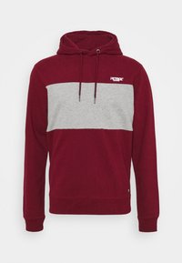 Sudadera color marrón con una franja horizontal gris en el pecho, con capucha ajustable y puños acanalados para un ajuste ceñido.