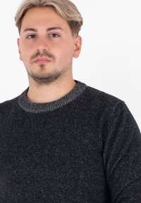 Maglione nero con un fitto intreccio, caratterizzato da un colletto e polsini a coste. Il materiale sembra morbido, con leggere variazioni di colore.