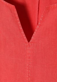 Nahaufnahme eines roten Stoffes mit einem V-Ausschnitt, sichtbaren Nähten und einer strukturierten Webart.