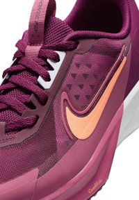 Scarpa atletica color malva con tomaia in mesh testurizzato, swoosh arancione a contrasto e linguetta imbottita. La suola è bianca con dettagli viola.