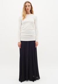 Vit långärmad åtsittande topp kombinerad med en flödande svart maxikjol, båda i mjuka tyger med en slät textur, vilket skapar en kontrasterande look.