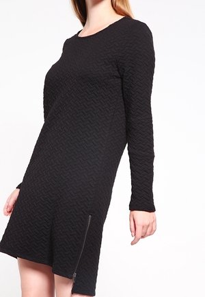 Abito nero a maniche lunghe con un motivo tessile testurizzato e una chiusura lampo laterale. Presenta un collo rotondo e una vestibilità ampia.