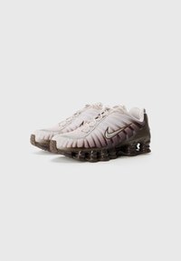 Nike Shox, s gradientovým jemným ružovým zvrškom, tmavohnedými plastovými prvkami, textúrovaným dizajnom a jedinečnou tlmiacou podrážkou pre podporu.