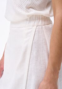 Witte linnen rok met subtiele textuur, voorzien van een tailleband en voorplooien. De stof is licht en soepel, perfect voor warm weer.