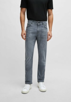 Jean en denim gris avec une coupe droite, poches avant et fermeture par bouton, associé à des baskets blanches et une chemise noire à manches courtes.