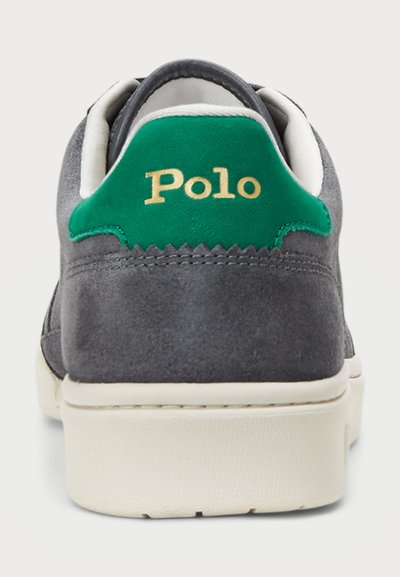 Sive sive tenisice s zelenim nubuk petnim detaljem na kojem piše "Polo" u zlatnoj boji. Bijela guma potplat, teksturirani detalji i minimalistički dizajn.