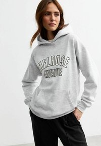 Gray sweatshirt with a hood, featuring "MELROSE AVENUE" in bold black text. Ribbed cuffs and a front pocket. Smooth texture.