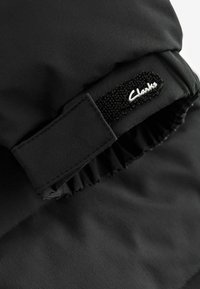 Svart tygpung med elastisk volang vid öppningen, försedd med ett svart kardborreband och vit "Clarks"-logotyp i kursiv stil.
