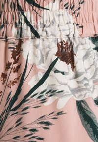 Tessuto floreale con base rosa, fiori bianchi e verdi e foglie marroni a contrasto. Tessitura morbida con arricciature nella parte superiore.