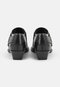 Scarpe con tacco in pelle nera, con punta arrotondata e tacco affusolato. Presentano una cerniera laterale e accenti in cintura con borchie metalliche.