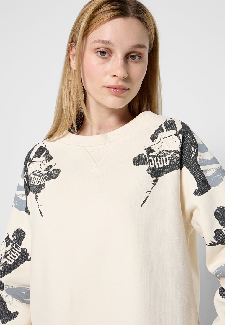 Cremfarbener Sweater mit schwarzen und grauen grafischen Druckmotiven von Figuren auf den Ärmeln, rundem Halsausschnitt, gerippten Bündchen und weicher Textur.