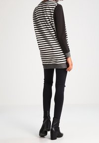 Schwarz-weiß gestreiftes Tunika mit langen Ärmeln, grauem Saum, kombiniert mit lässigen schwarzen Skinny-Jeans und schwarzen Stiefeletten.