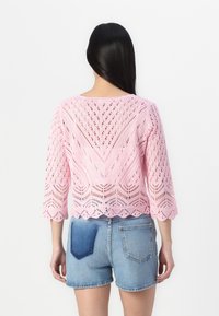 Rosa stickad tröja med spetsmönster och trekvartslånga ärmar, tillsammans med denimshorts med en lapplagd bakficka.