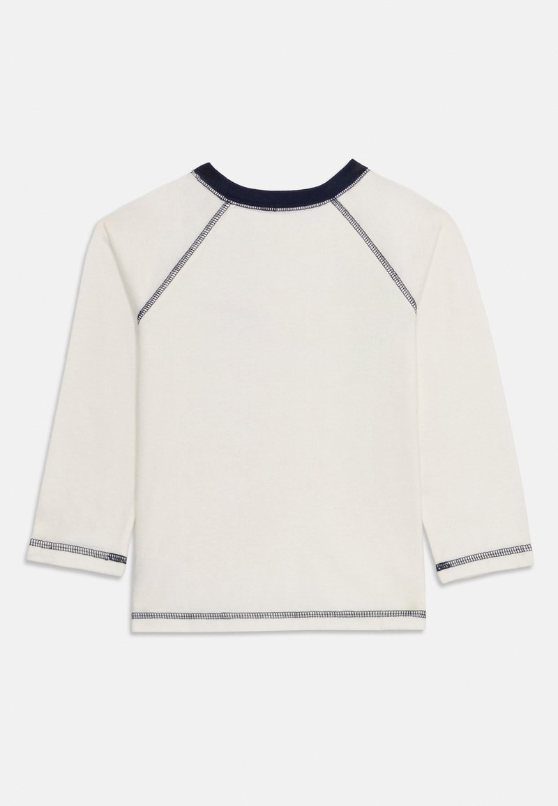 Camisa blanca de manga larga con cuello y puños de canalé en navy, con costuras de contraste a lo largo de las costuras y dobladillos.