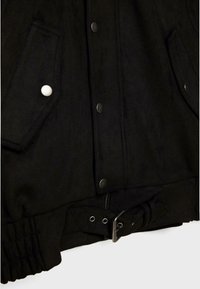 Gros plan sur une veste noire montrant des boutons pression, des poches avant avec rabats et une ceinture réglable avec boucle en métal à la taille.