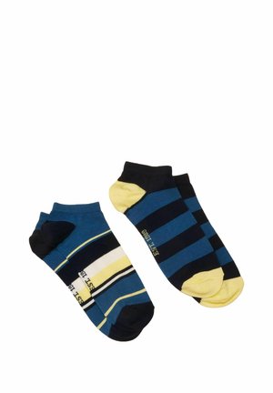 Deux paires de chaussettes courtes avec des rayures bleues, noires, blanches et jaunes, une paire avec talons et orteils jaunes sur un fond blanc.