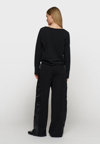 Zwart loungewearset bestaande uit een casual sweatshirt en wijde broekspijpen. Satijnen accenten aan de zijkant van de broek. Zachte textuur en een minimalistisch design.