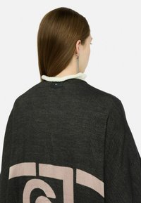 Poncho nero e beige con motivo a stampa e finitura testurizzata, dotato di un colletto bianco e di un bottone sul retro.