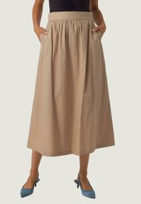 Beige, mid-length kjol med elastisk midja, sidofickor och en slät yta. Bärs med ljusblå, spetsiga skor.
