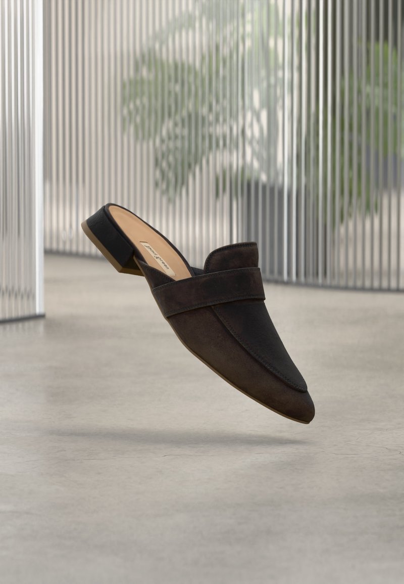 Mocassins en cuir marron foncé à enfiler, avec un petit talon bloc, un bout pointu et un détail de bride, flottant au-dessus d'un sol gris clair.