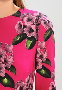 Rosa Kleid mit Blumenmuster, das große, illustrierte rosa Blumen und grüne Blätter zeigt. Glatte Textur und kurze Ärmel.