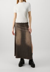 Biały prążkowany top z krótkim rękawem i falowanymi krawędziami, zestawiony z długą brązową spódnicą z gradientem i wysokim rozcięciem. Czarne botki na platformie.