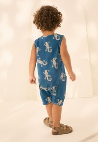 Blå ærmeløs romper med firbenmønster i beige. Fremstillet i blødt stof, med sidelommer og afslappet pasform. Brune sandaler bæres.