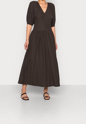 Braunes, strukturiertes Maxikleid mit V-Ausschnitt und Puffärmeln, ausgestattet mit einem taillierten Oberteil und einem fließenden, gerafften Rock. Kombiniert mit schwarzen Sandalen.