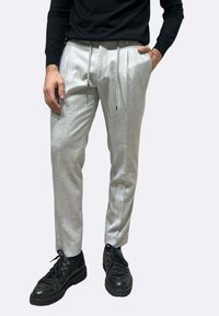 Pantaloni su misura grigio chiaro con una texture sottile, vita con coulisse e tasche laterali, abbinati a scarpe nere con lacci.