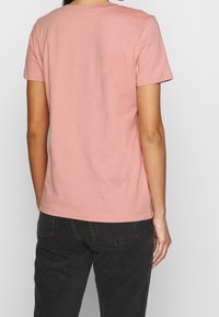 Camiseta de manga corta y cuello redondo en suave algodón de color rosa claro, con un corte recto y detalles de costura mínimos en el dobladillo y las mangas.