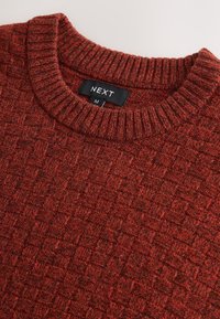 Raudonas megztas megztinis su įgilintu langelių raštu, su riboto iškirptės apykakle. Etiketėje užrašyta „NEXT“ ir dydis „M“.